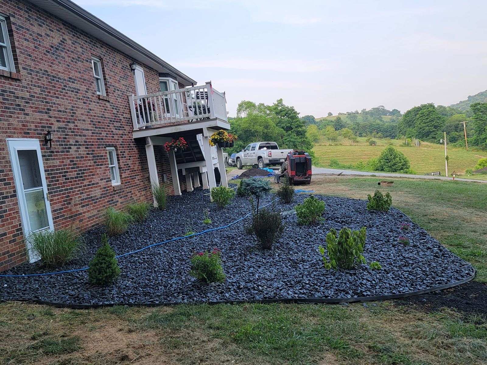 Black river rock landscape bed with new plantings at a brick home